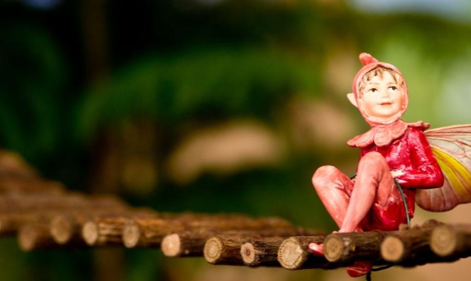 A small fairy sits on a swinging bridge made of twigs