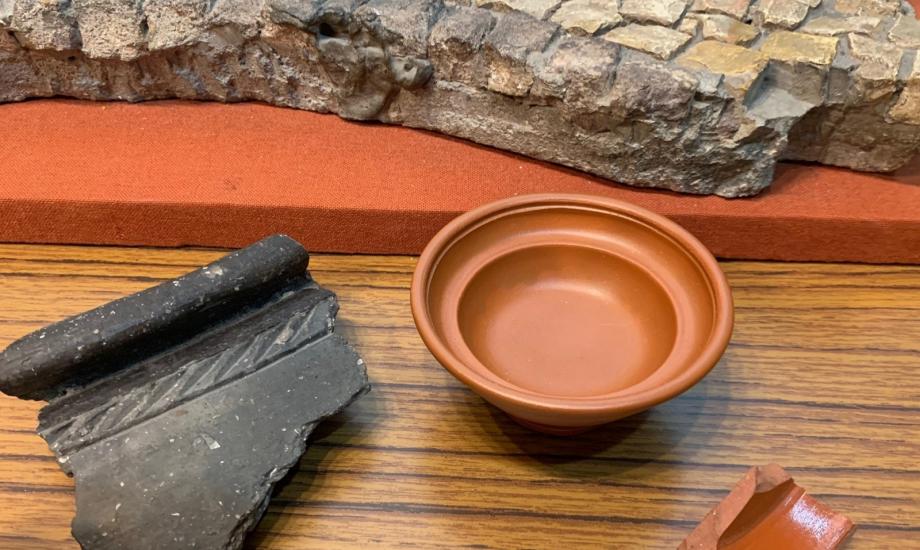 colour image of Roman terracotta pot, fragments of pots and mosaic in background