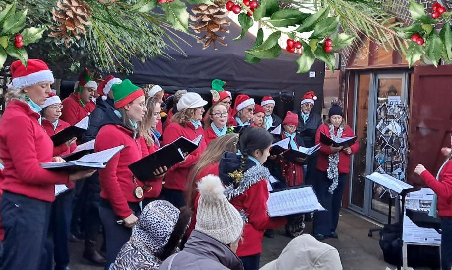 Choir stand in courtyard wearing santa hats and reading from hymn sheets