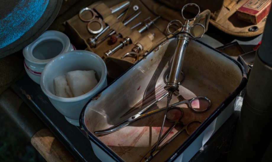 Photo of old-fashioned surgery tools in a tray against a background of old manuscripts and bottles