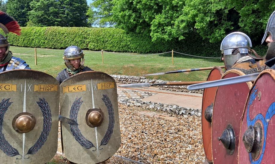 Two Roman re-encting soldiers face off 3 re-enacting Saxon warriors in full costume, outside 