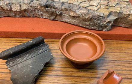 colour image of Roman terracotta pot, fragments of pots and mosaic in background