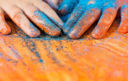 Small hands of toddler spreading blue glitter into orange paint